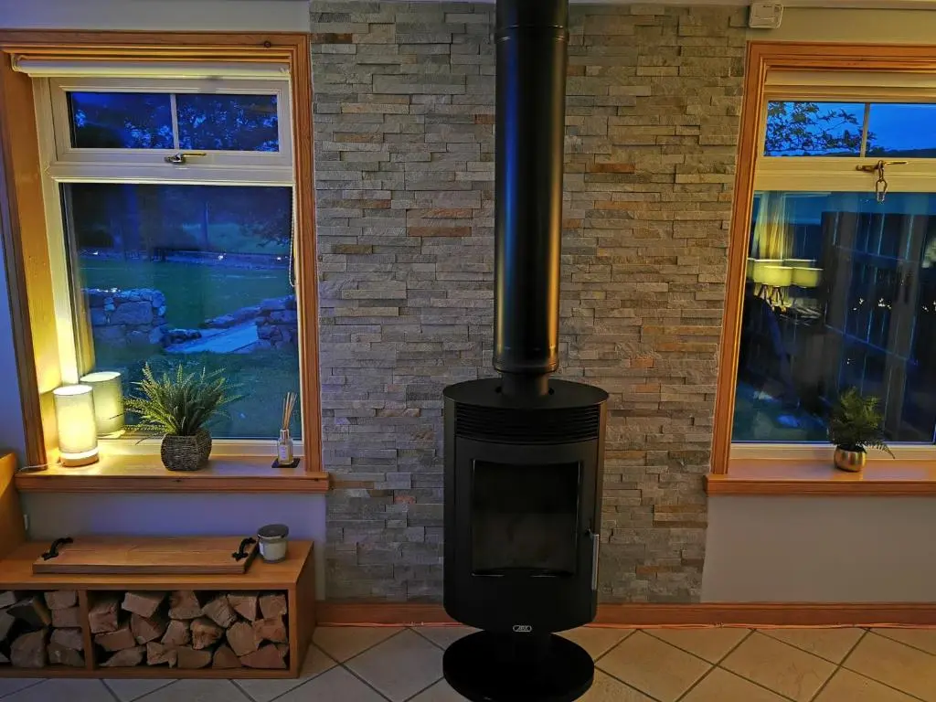 a wood stove in a room with two windows at Private peacefull pet friendly converted country cottage in Keig