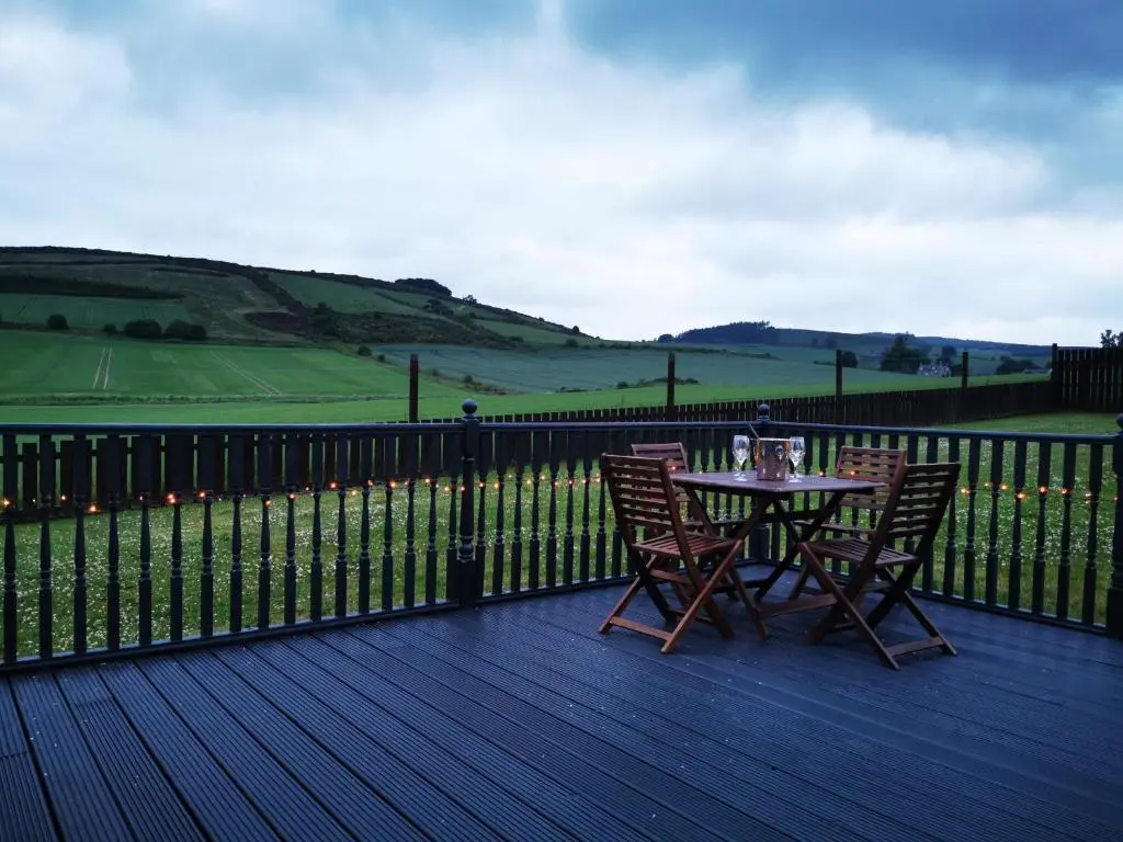a table and chairs on a deck with a fence at Private peacefull pet friendly converted country cottage in Keig
