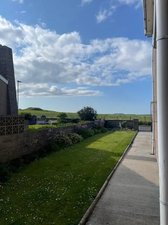 a walkway next to a wall with a green lawn at Impala Guest House in Wick