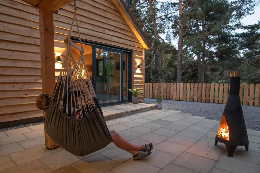 a person sitting in a hammock in front of a house at Arbor Nethy Bothy in Cairngorms National Park in Nethy Bridge