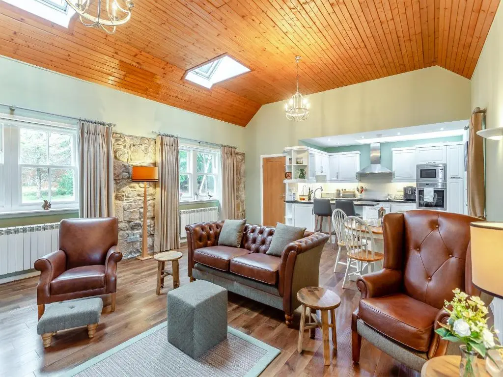 a living room with leather furniture and a kitchen at The Bothy in Lochend