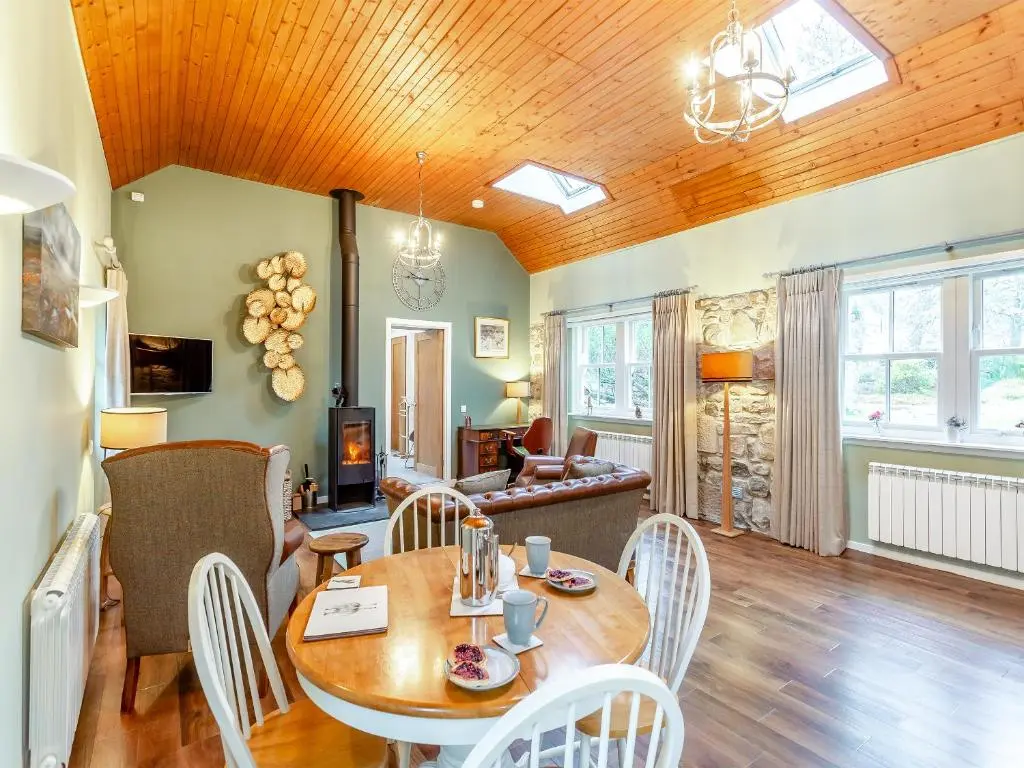 a dining room and living room with a wooden ceiling at The Bothy in Lochend