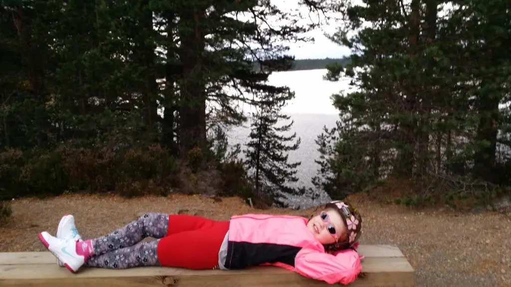 a little girl laying on a bench near the water at Cluny Mains in Newtonmore