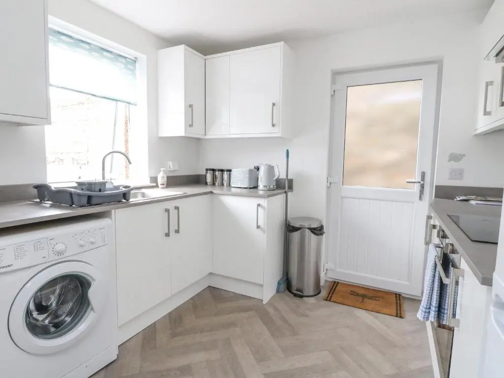 a white kitchen with a washing machine and a sink at Anchor Cottage in Elgin
