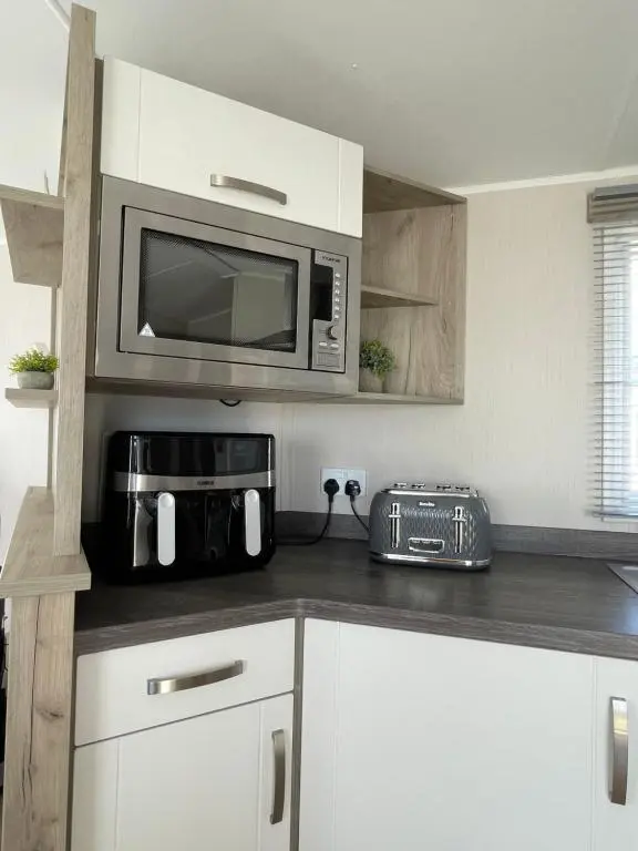a kitchen with white cabinets and a microwave at Fairview Caravan Hire in Lossiemouth
