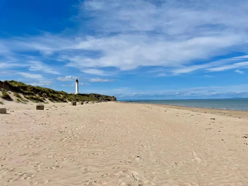 a sandy beach with a lighthouse in the distance at Fairview Caravan Hire in Lossiemouth