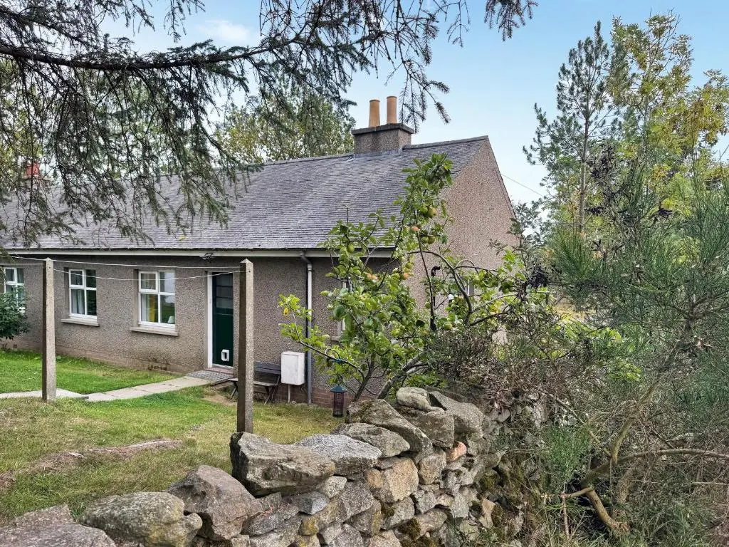a house with a stone wall in front of it at Damil Cottage - Uk44789 in Bridge of Alford