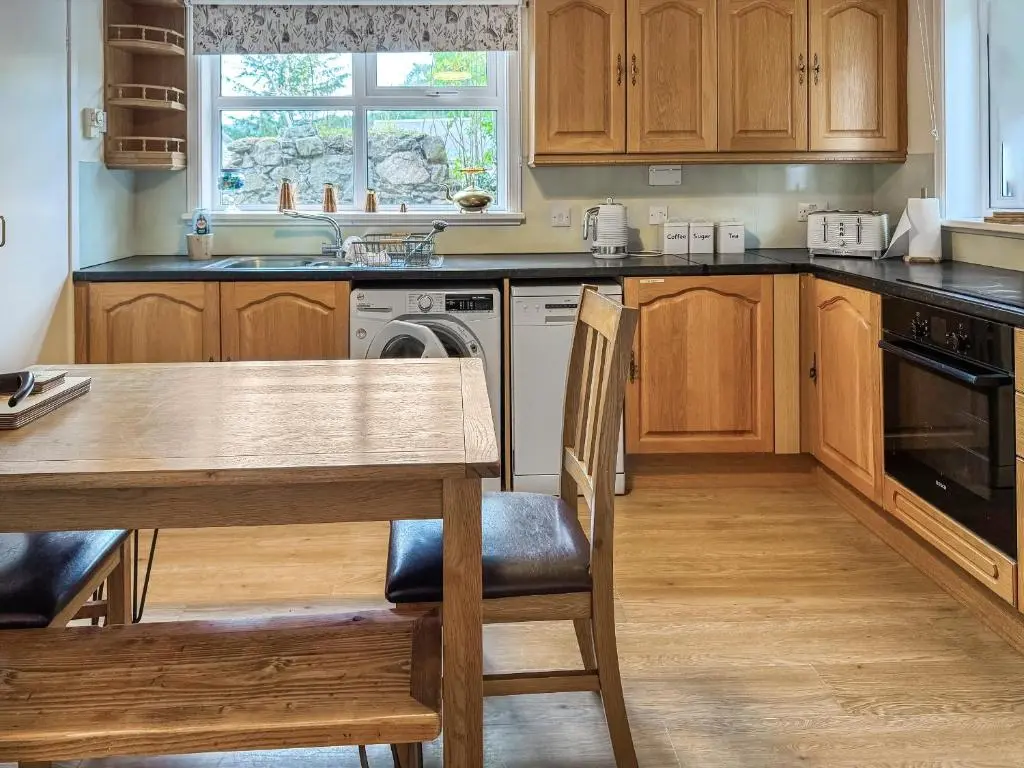 a kitchen with wooden cabinets and a table and a sink at Damil Cottage - Uk44789 in Bridge of Alford