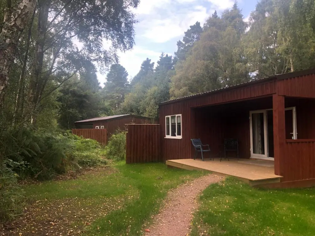 a small red building with a porch and a chair outside at The South Cabin at Easter Arr in Nairn