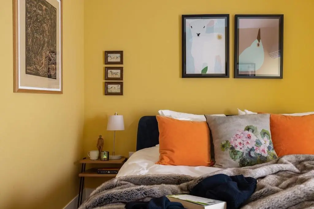 a bedroom with yellow walls and a bed with orange pillows at The Corner House in Banchory