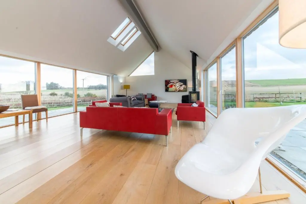 a living room with a red couch and a white chair at The Den, Architect Designed Barn, Beautiful Location in Kirkton of Skene