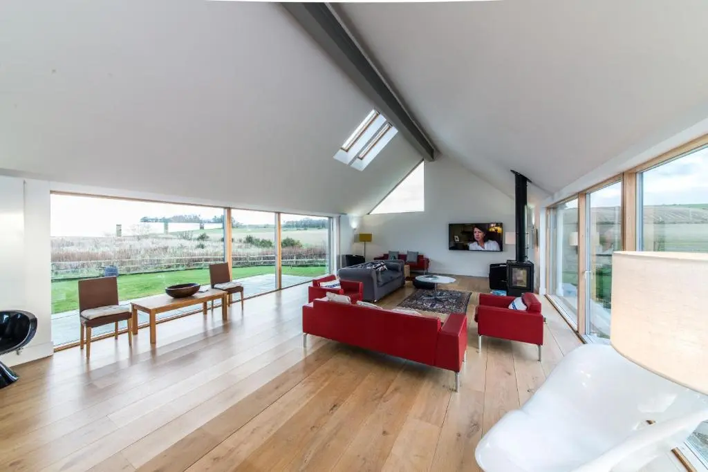 a living room with red furniture and large windows at The Den, Architect Designed Barn, Beautiful Location in Kirkton of Skene