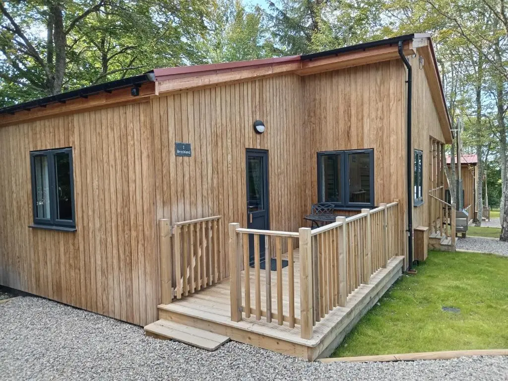 a wooden cabin with a porch and a deck at Breckland Lodge 1 with Hot Tub in Belladrum