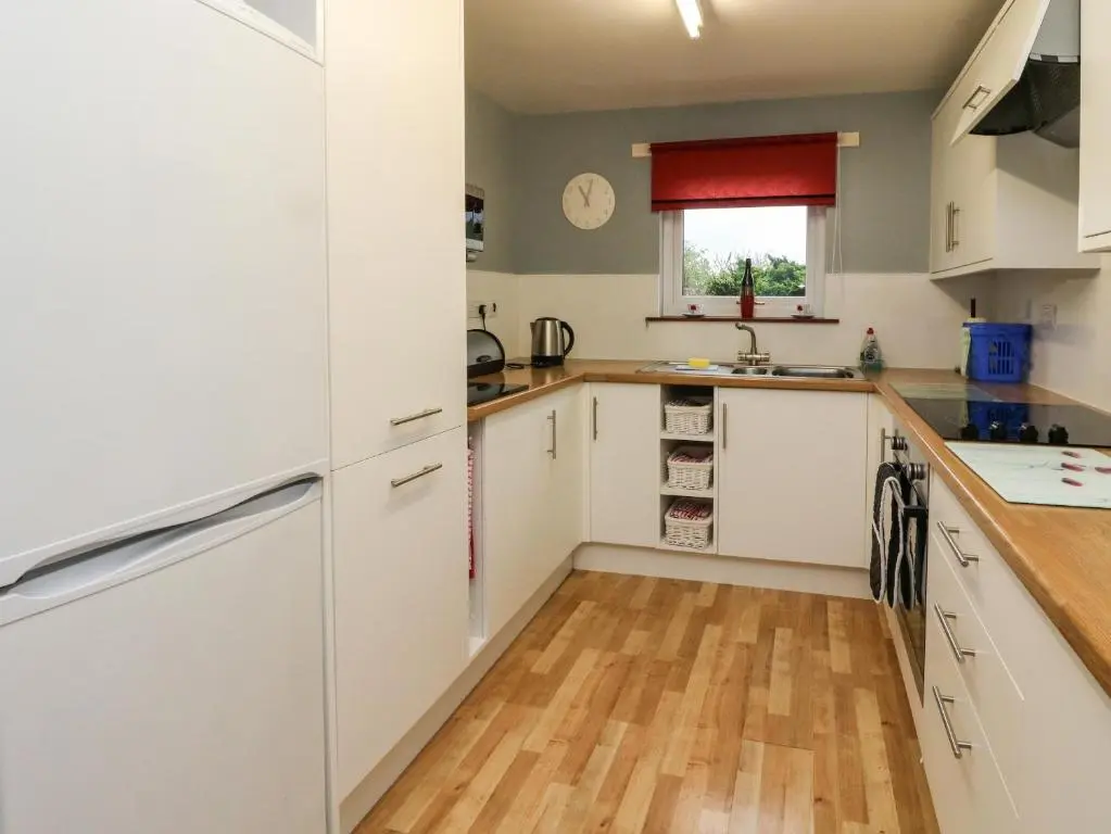a kitchen with white cabinets and a wooden floor at Bide-a-While in Marnoch