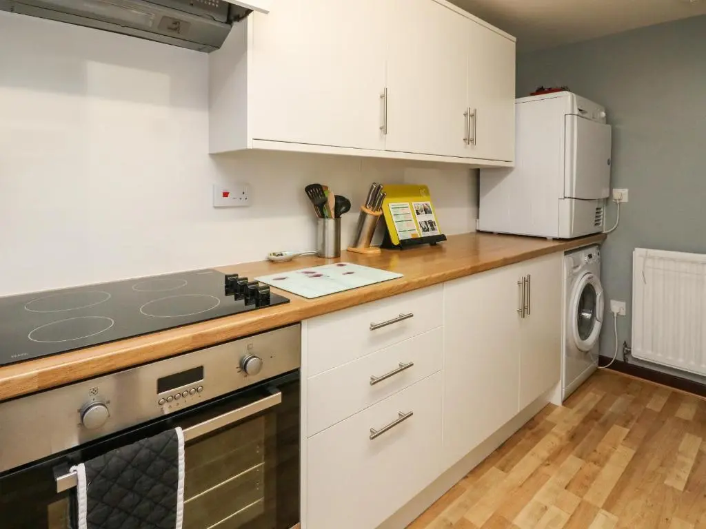 a kitchen with white cabinets and a washer and dryer at Bide-a-While in Marnoch