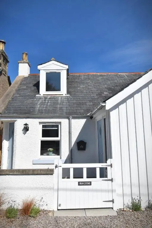 a white house with a white fence in front of it at Dram Cottage, Findhorn Bay in Forres
