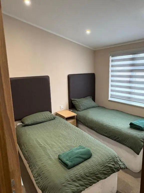 a bedroom with two beds with green sheets and a window at Clochnaben lodge in Strachan