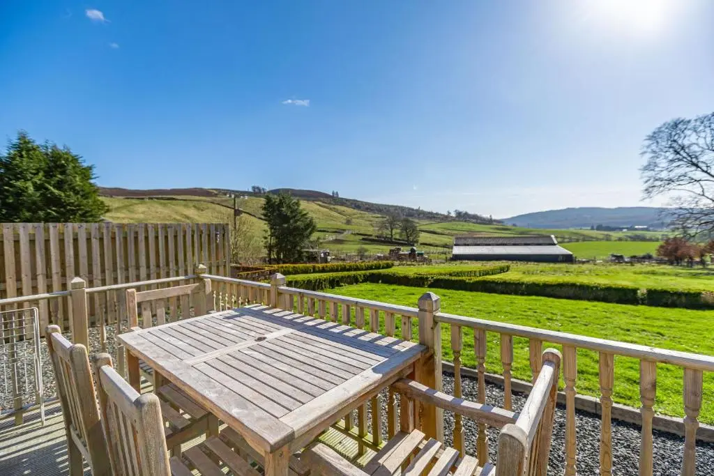 a wooden table and chairs on a deck with a fence at Gardener\u2019s Cottage with Hot Tub in Blairgowrie