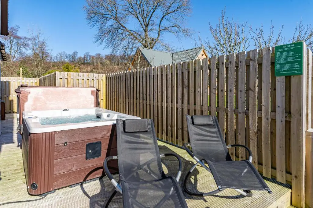 two chairs and a grill on a deck with a fence at Gardener\u2019s Cottage with Hot Tub in Blairgowrie
