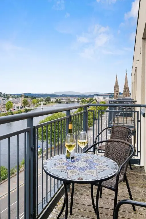 a table with two glasses of wine on a balcony at By the Bridge by Toppo in Inverness
