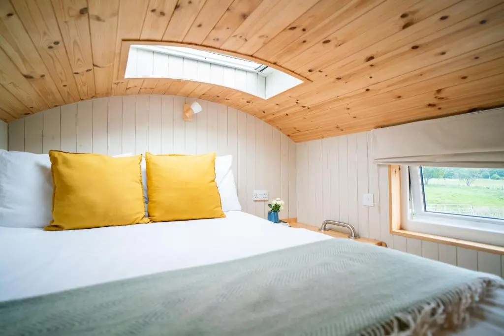 a bedroom with a bed with yellow pillows and a window at Ailsa- Enchanting Tiny House with wood burner and hot tub in Cairngorms in Ballater