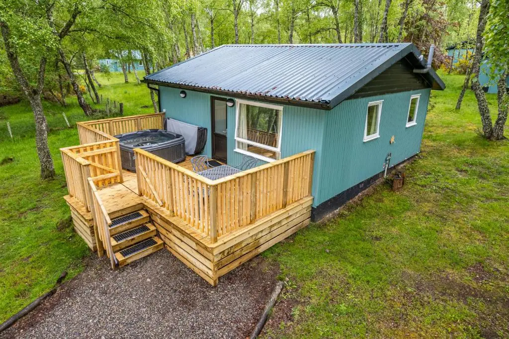 a small blue house with a large deck at Bracken Lodge 15 with Hot Tub in Belladrum