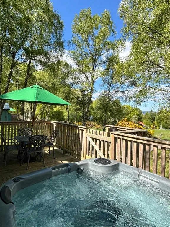 a hot tub on a deck with a table and an umbrella at Bracken Lodge 15 with Hot Tub in Belladrum