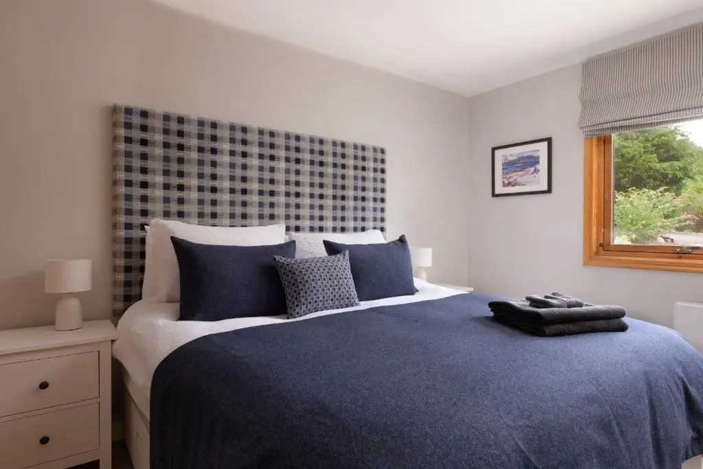 a bedroom with a large bed with blue sheets and a window at Ballater Bungalow - 4 bed - Beautiful Garden in Ballater