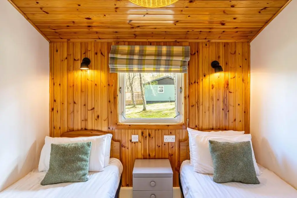 two beds in a small room with a window at Heather Lodge 1 with Hot Tub in Belladrum