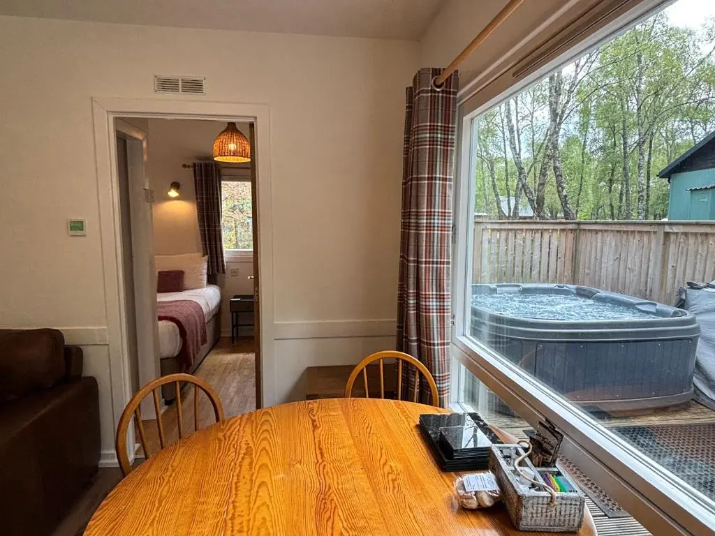 a room with a table and a large window with a tub at Heather Lodge 3 with Hot Tub in Belladrum