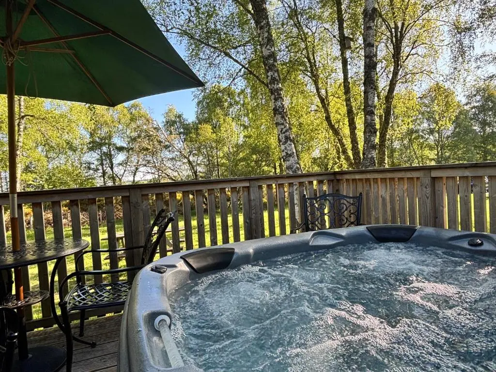 a hot tub on a deck with a table and an umbrella at Heather Lodge 10 with Hot Tub in Belladrum