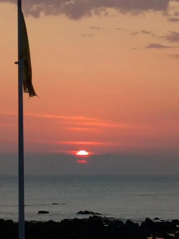 a sunset over the ocean with a flag at Craigmile Cottage in Fraserburgh