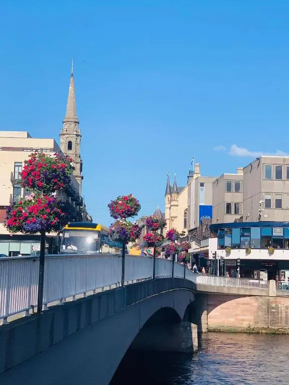 a bridge over a river with flowers on trees at Scardroy Homes Inverness - Central 2 Bedroom with Parking WiFi Smart TVs Sleeps up to 6 in Inverness
