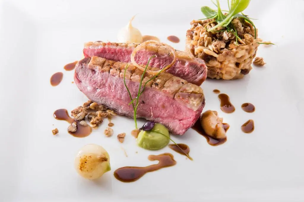 a piece of meat on a white plate with nuts at The Glenmoriston Townhouse Hotel in Inverness