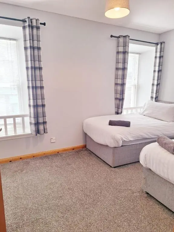 two beds in a room with two windows at 3 Bedroom Townhouse on NC500, Wick, Highland in Wick