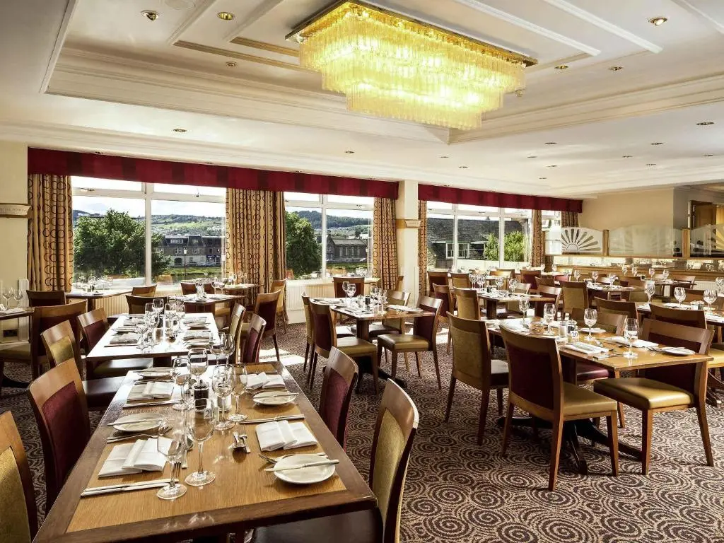 a restaurant with tables and chairs and a chandelier at Mercure Inverness Hotel in Inverness