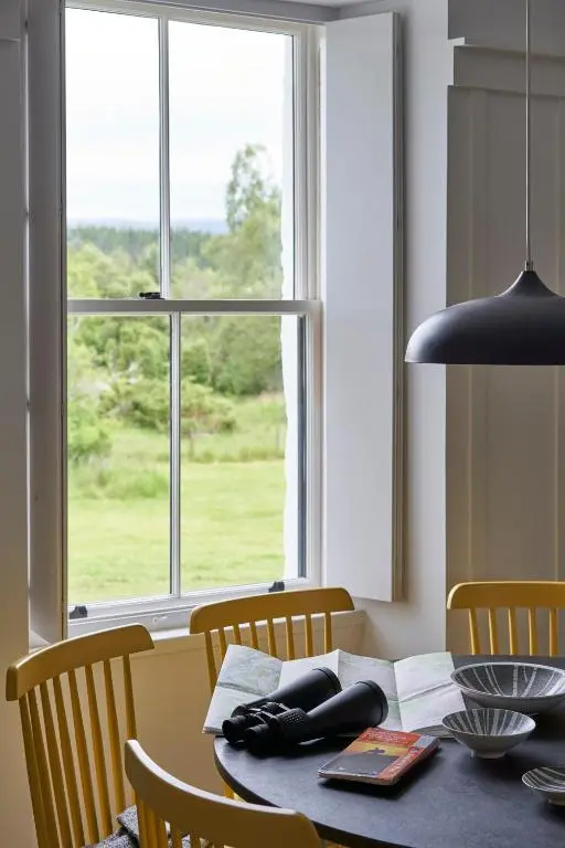 a dining room table with chairs and a large window at Achnahatnich House in Aviemore