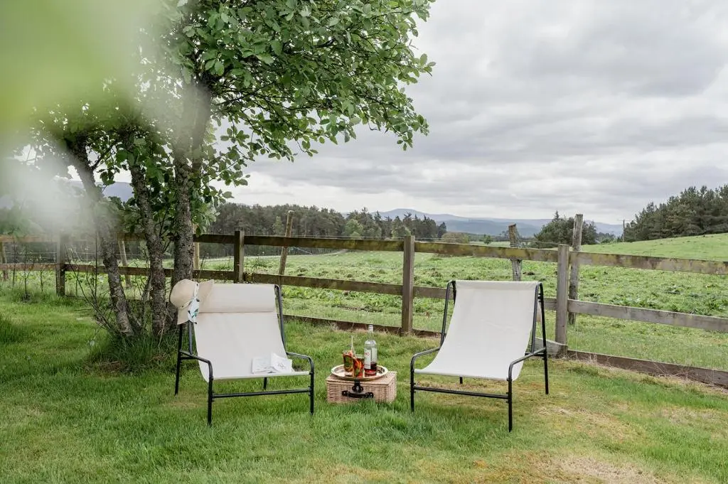two chairs sitting in the grass next to a fence at Gleann Cottage - Seasgair Lodges in Kincraig
