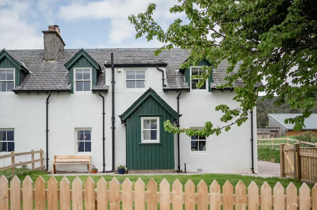 a white house with a green door and a fence at Beinn Cottage - Seasgair Lodges in Kincraig