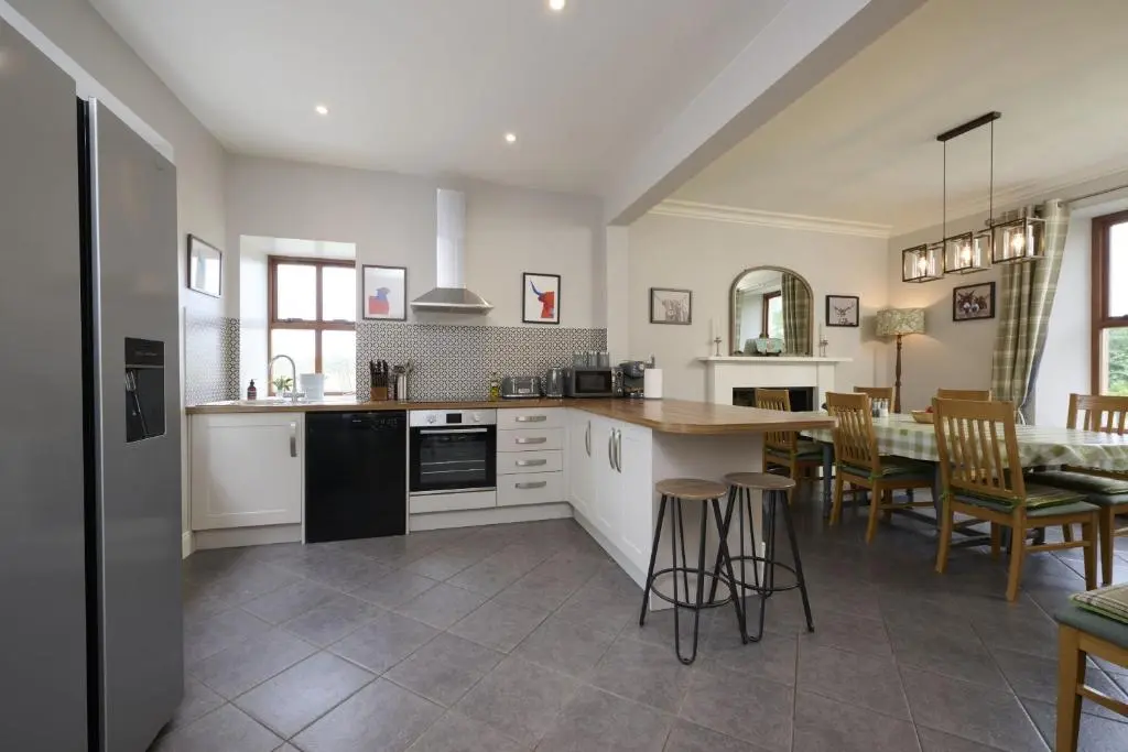 a kitchen with white cabinets and a table and chairs at Dunaincroy Farmhouse in Inverness