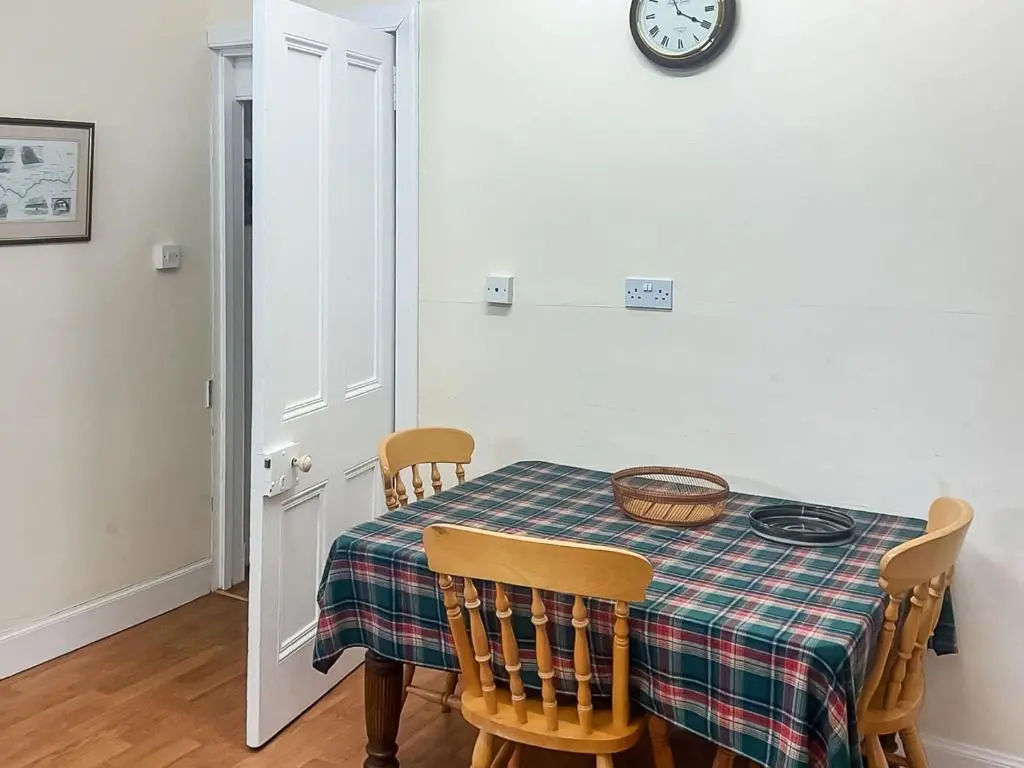 a dining room table with chairs and a clock on the wall at Gleneffock Farmhouse in Tarfside