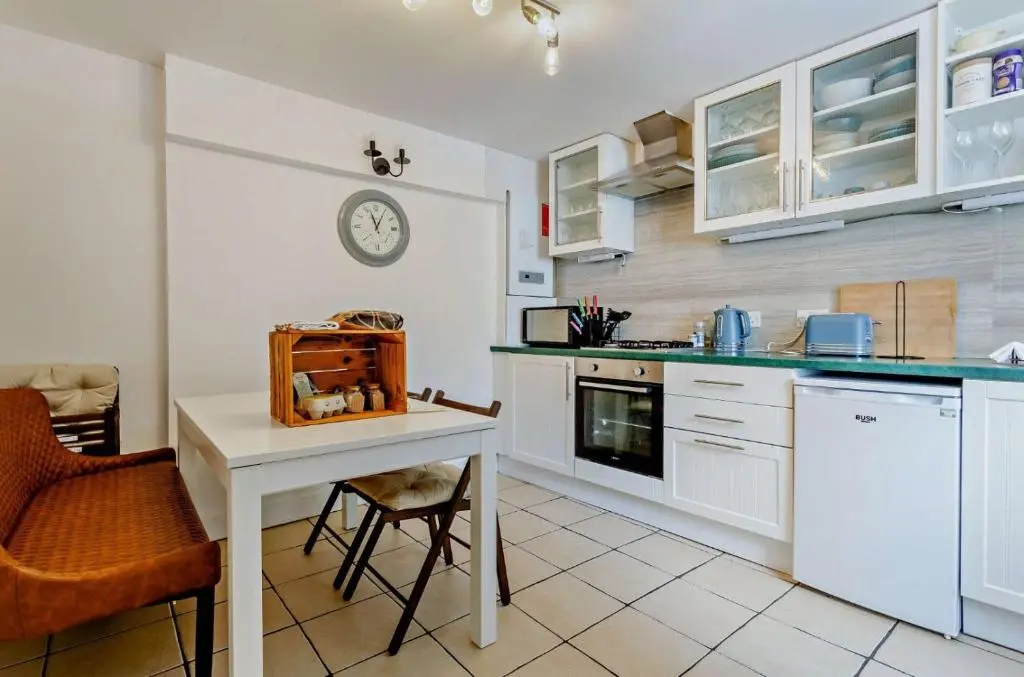 a kitchen with white cabinets and a table and a clock at Jacobite's Retreat, 17th century cottage in the heart of Inverness in Inverness