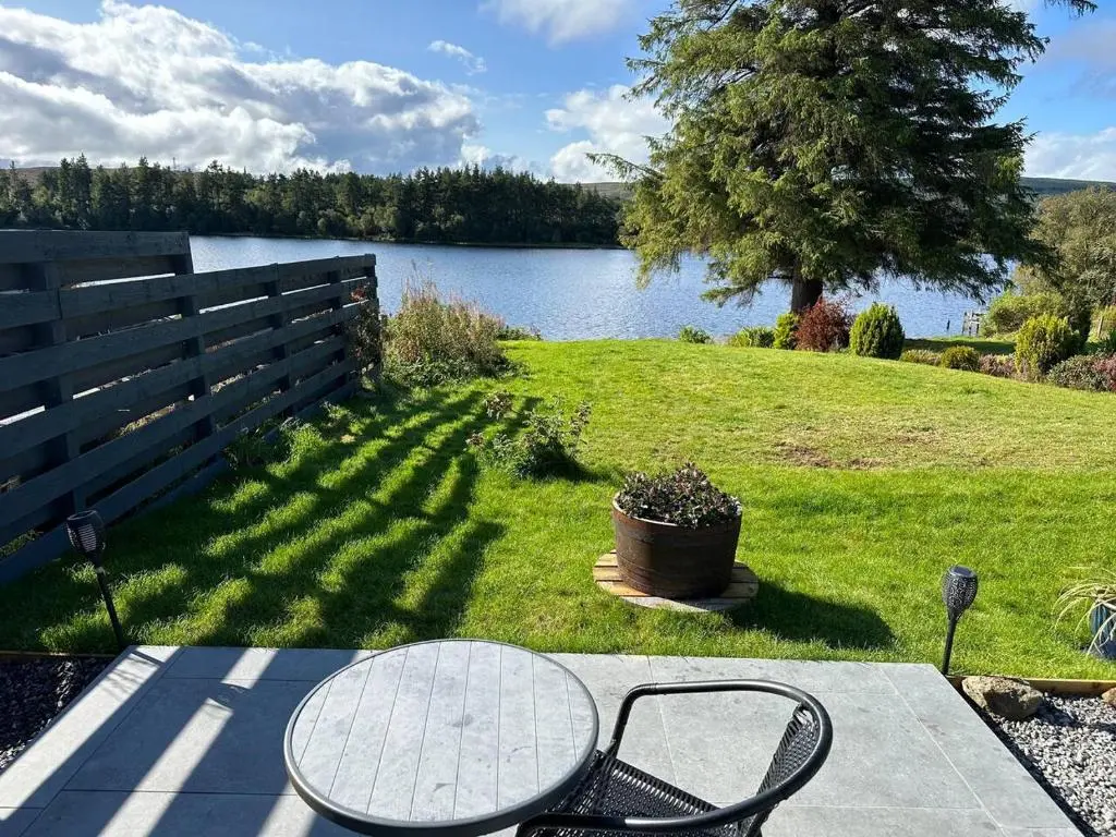 a table and chairs on a patio near a lake at Lochside Lodge Pod in Lairg