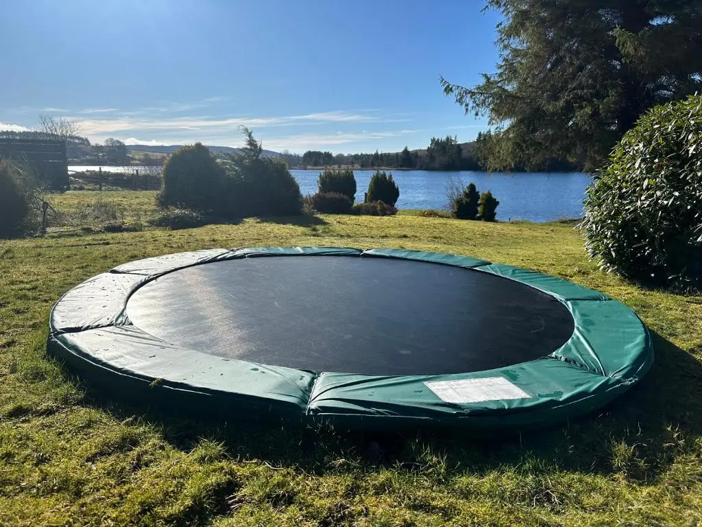 a trampoline in the grass next to a lake at Lochside Lodge Pod in Lairg