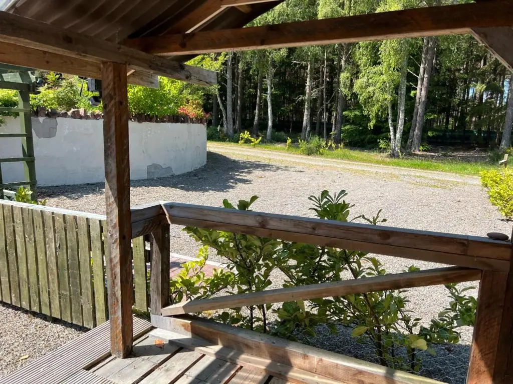 a wooden porch with a wooden fence and trees at Birchwood Cottage in Tore