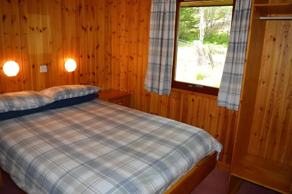 a bed in a wooden room with a window at Reuben's Highland Retreat - Speyside in Carrbridge