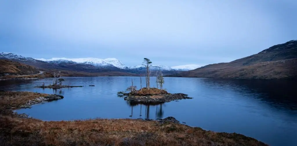 a small island in a lake with mountains in the background at The High Croft in Rogart