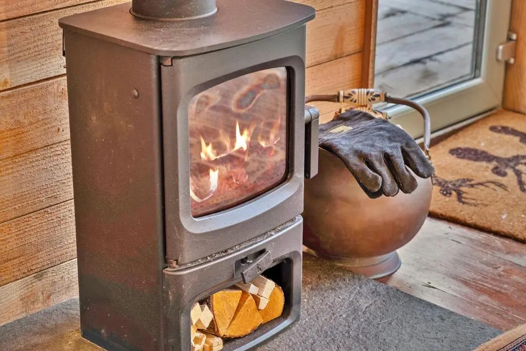 a wood burning stove with a person wearing a glove at Finest Retreats - Cosagach Falls Cabin in Kiltarlty