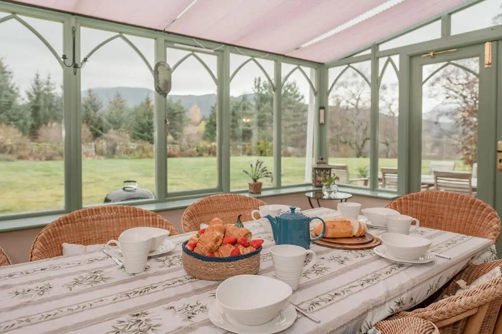 a table in a conservatory with a table with food on it at Milton Lodge - Seasgair Lodges in Newtonmore