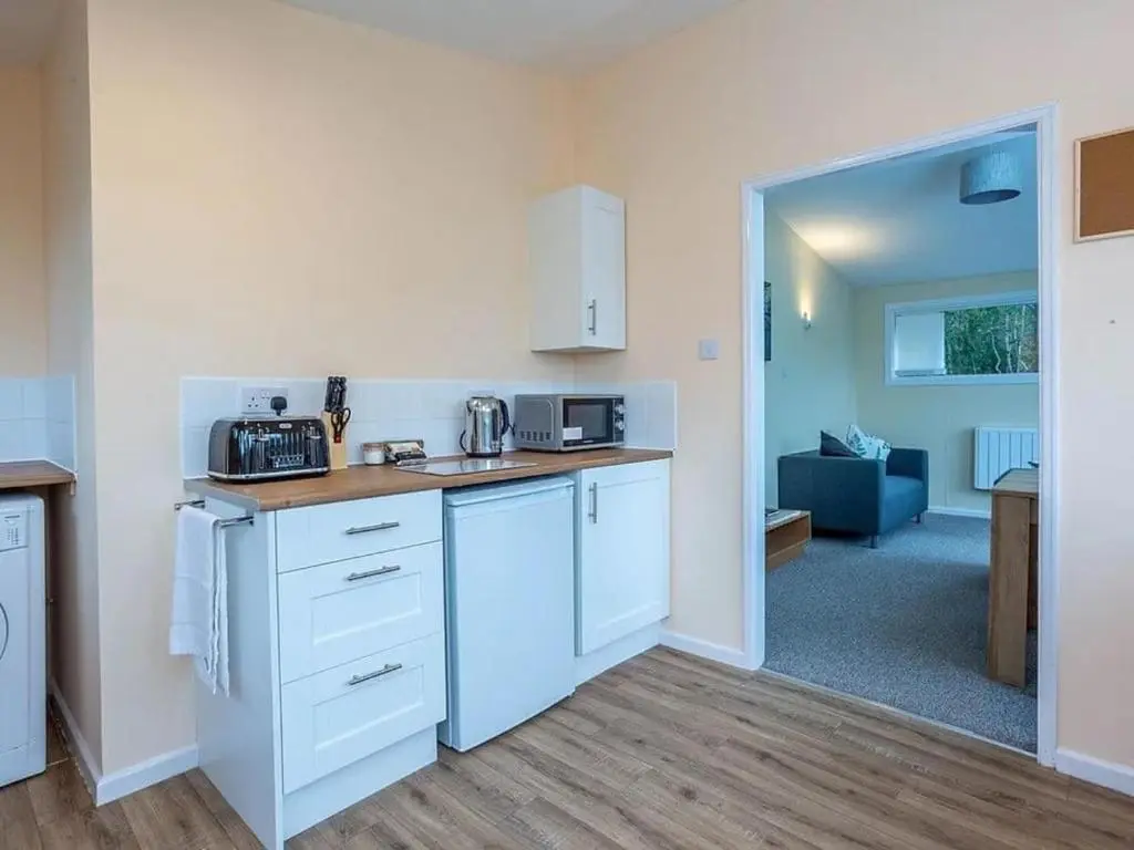 a kitchen with white cabinets and a living room at Bridgend Chalet on Reelig Estate in Kirkhill